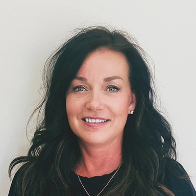 Front Desk Receptionist Jeri Smiling In Front Of Off-White Wall