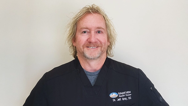 Chiropractor Jeff Gray Smiling In Front Of Off-White Wall